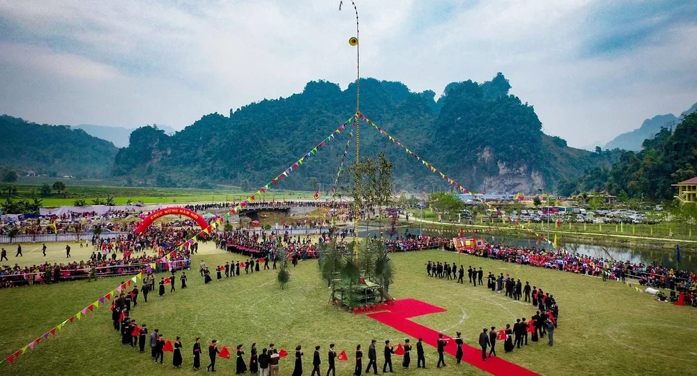 Vue aérienne du terrain de la fête de Lồng Tồng avec un mât de lancer de còn (cây còn) au centre et une procession d'habitants en costume traditionnel.
