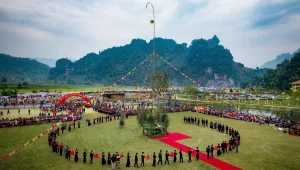 Vue aérienne du terrain de la fête de Lồng Tồng avec un mât de lancer de còn (cây còn) au centre et une procession d'habitants en costume traditionnel.