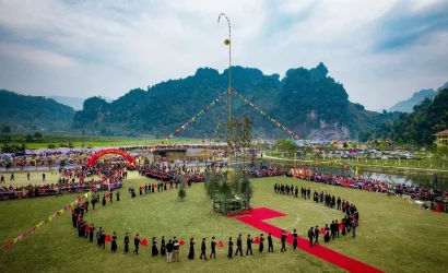 Vue aérienne du terrain de la fête de Lồng Tồng avec un mât de lancer de còn (cây còn) au centre et une procession d'habitants en costume traditionnel.