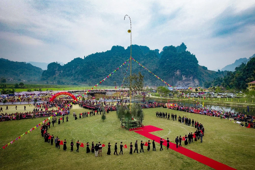 Vue aérienne du terrain de la fête de Lồng Tồng avec un mât de lancer de còn (cây còn) au centre et une procession d'habitants en costume traditionnel.
