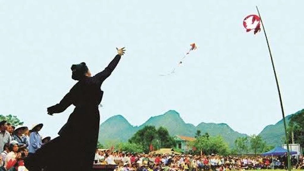 Une femme en costume traditionnel lance le quả còn (balle d'étoffe) à travers le cerceau sommet du mât sous les encouragements de la foule.