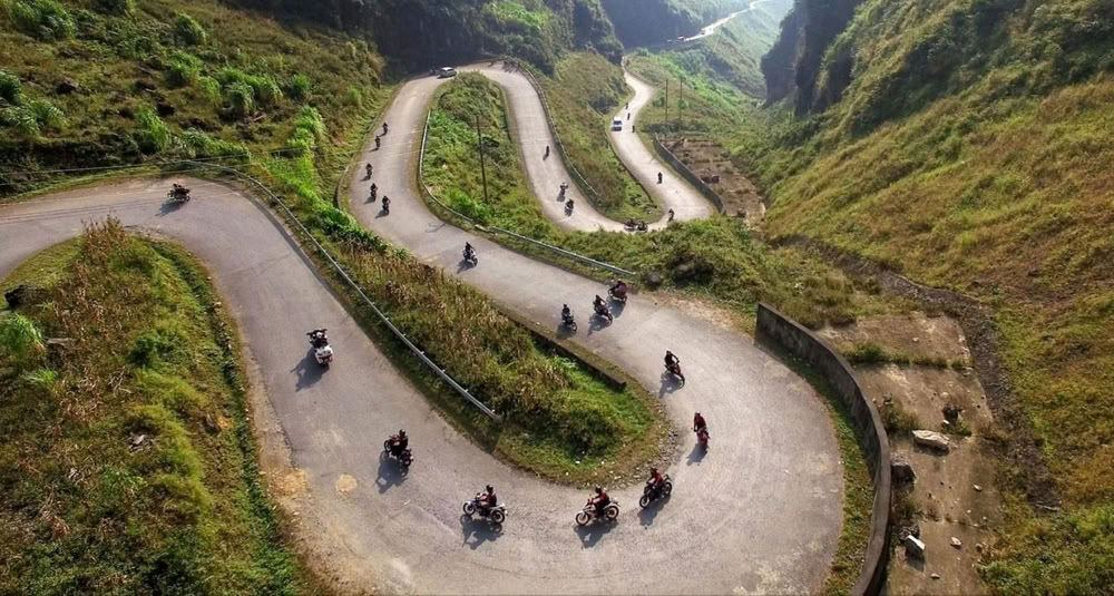 Une route montagneuse sinueuse à Hoang Su Phi sillonnée par un groupe de motocyclistes en plein voyage.