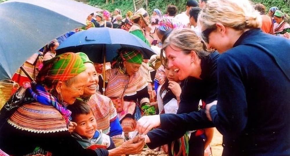 Des touristes étrangères échangeant de manière amicale avec des femmes H'Mong au marché de Bắc Hà.