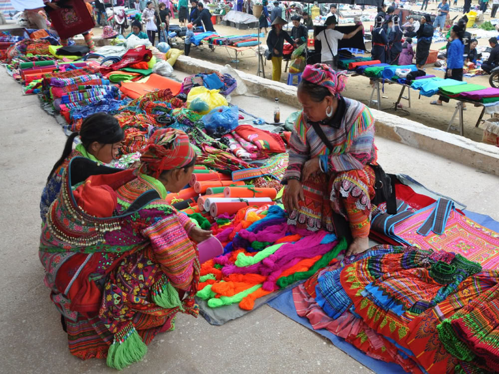 Femmes d'ethnies minoritaires choisissant des fils et tissus brodés colorés au marché de Mường Hum.