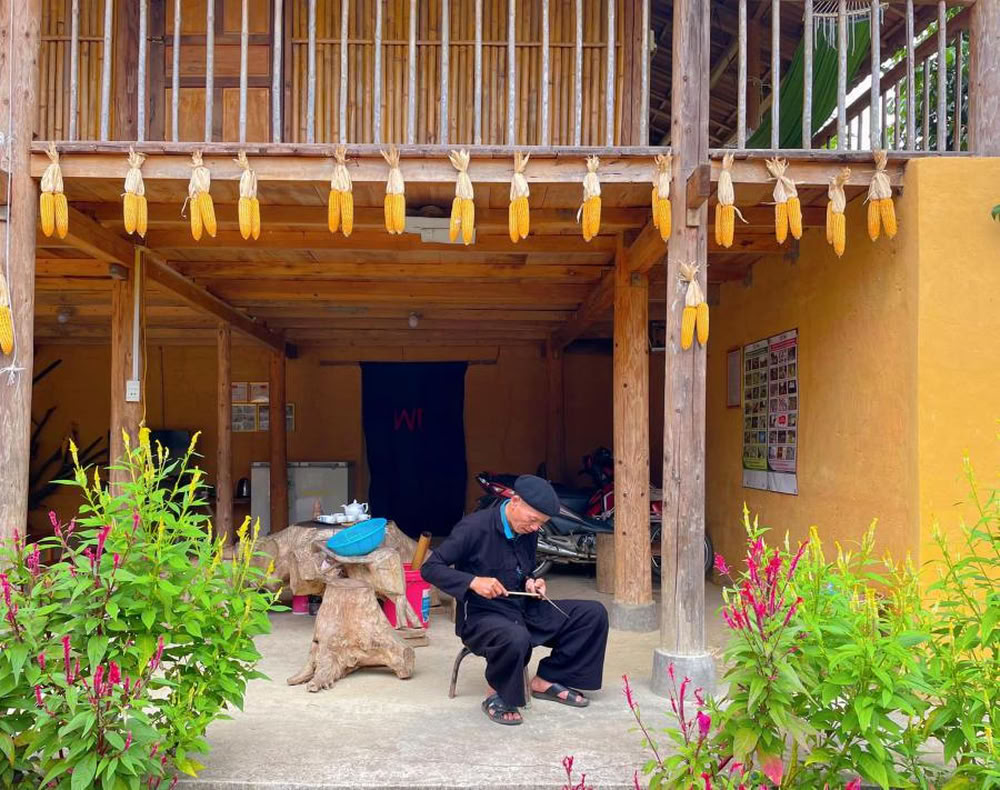 Un homme âgé de l'éthnie locale travaillant paisiblement devant sa maison en bois sur pilotis.